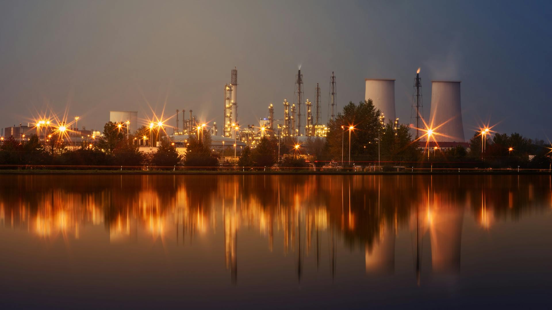 Oil refinery illuminated at night reflected in water — oil and gas fundamentals